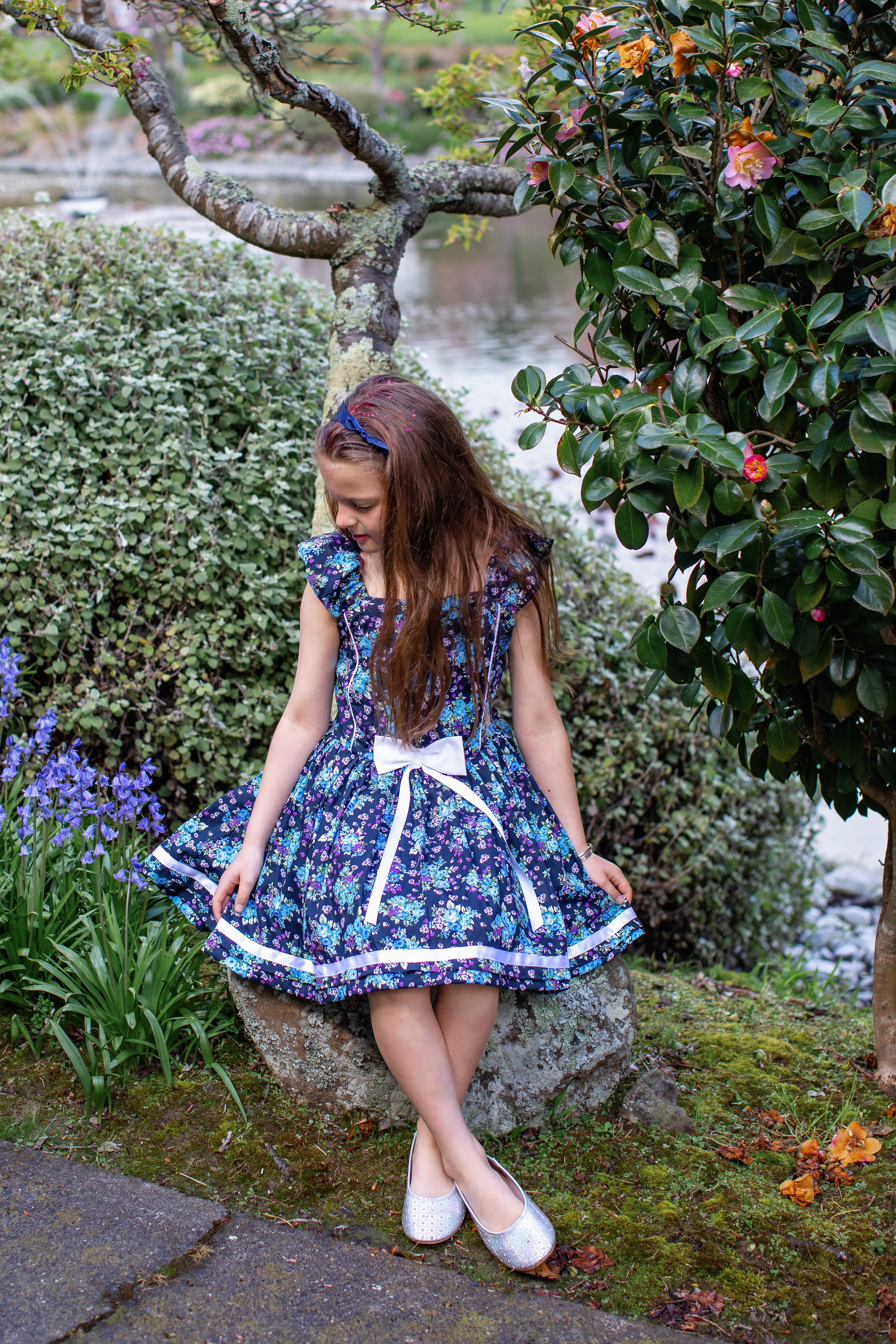 “Exclusive Blueberry little girls' party dress by Vanessa Lynne, made with high-quality printed cotton, featuring piping, ribbon accents, and a cute bow at the center. Fully lined for extra puff, perfect for twirling at any occasion.”